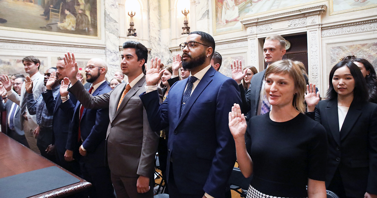 three rows of individuals hold their hands up to take an oath