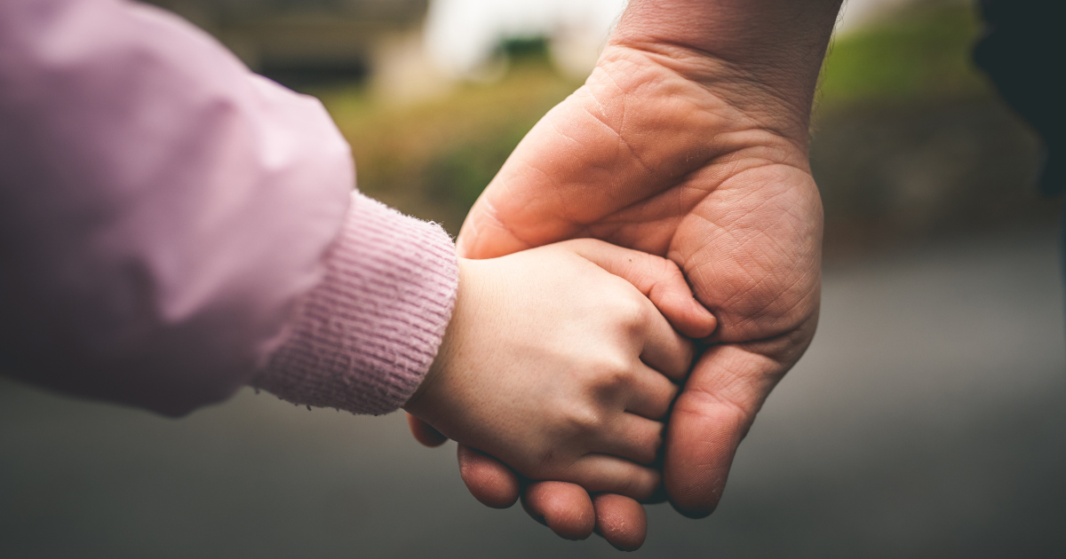 Close Up Of An Adult Man Gripping A Child's Hand As They Walk On An Overcast Day, With The Distance Out Of Focus