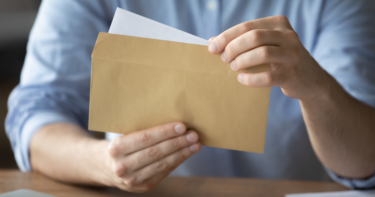 Medium Close Up Of A Man In A Sport Shirt, His Sleeves Rolled Up, Placing A Piece of Paper Into A Brown Letter-Sized Envelope