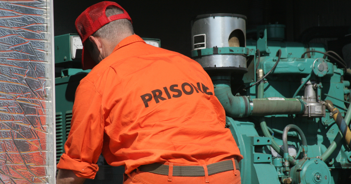 Man In Orange Prison Jumpsuit Bending Over A Machine