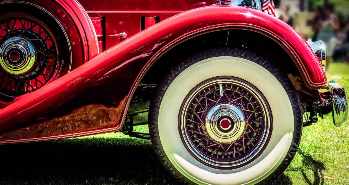 Medium Close Up Profile Of The Front Of A Red Luxury Car From The 1930s, With Gleaming Chrome And A While Wall Tire And A Swooping Wheel Cover