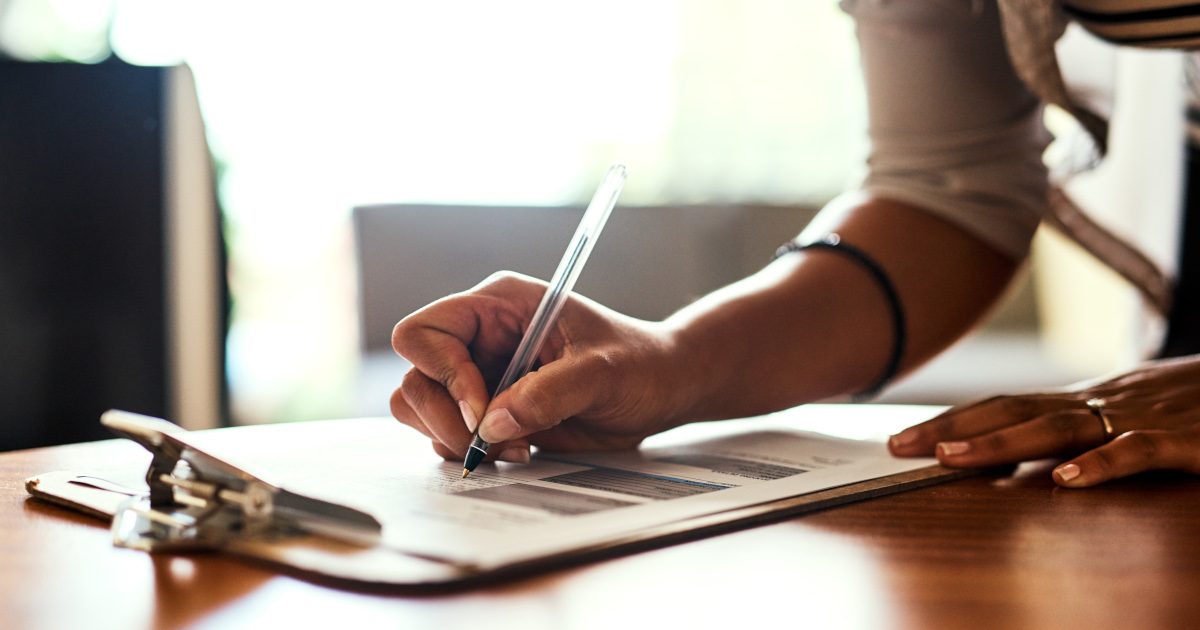 Closeup of A Woman Bending Over A Table To Fill Out A Form Attached To A Clipboard