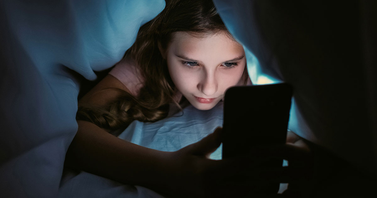 girl under the bedcovers looking at a phone