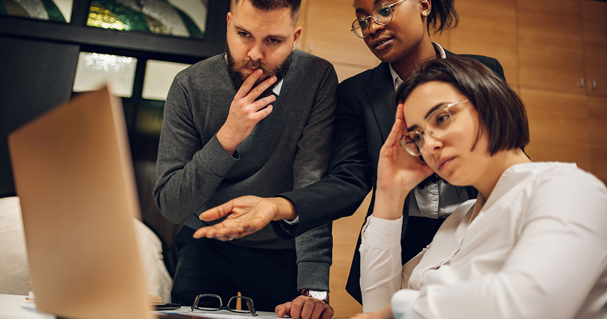 Team of office workers looking frustrated standing over computer